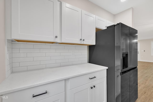 kitchen featuring white cabinetry, light stone counters, black refrigerator with ice dispenser, light hardwood / wood-style floors, and decorative backsplash