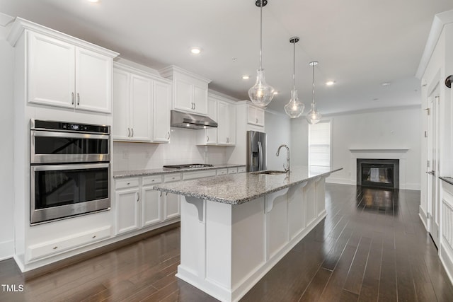 kitchen with a kitchen bar, an island with sink, white cabinets, and appliances with stainless steel finishes