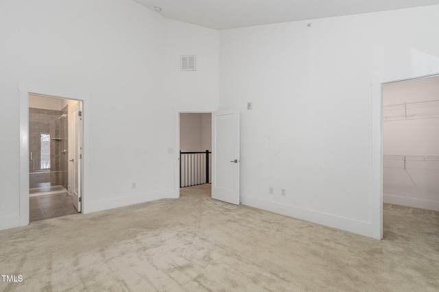 unfurnished bedroom featuring ensuite bathroom, a spacious closet, high vaulted ceiling, a closet, and light colored carpet