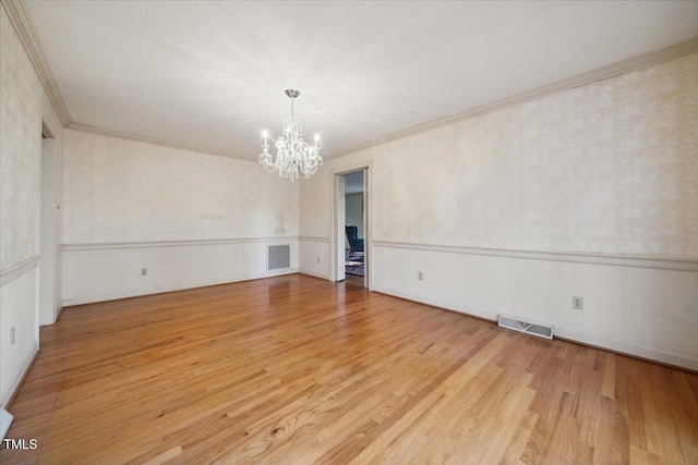 empty room with crown molding, light hardwood / wood-style flooring, and a chandelier