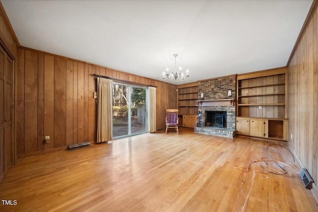 unfurnished living room featuring an inviting chandelier, a fireplace, light hardwood / wood-style floors, and wood walls