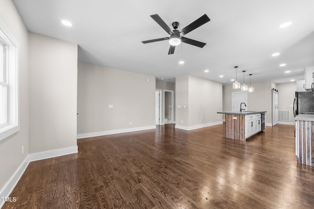 unfurnished living room featuring a barn door, ceiling fan, dark hardwood / wood-style flooring, and sink