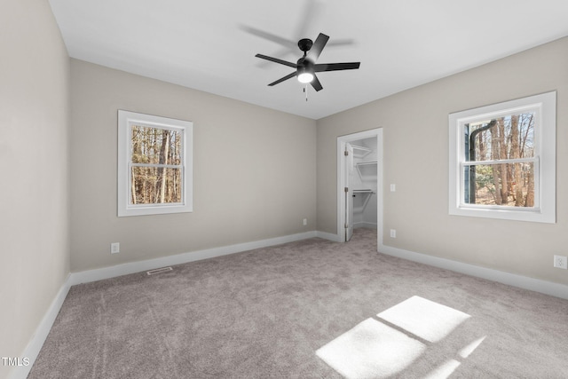 unfurnished bedroom featuring ceiling fan, a walk in closet, a closet, and light carpet