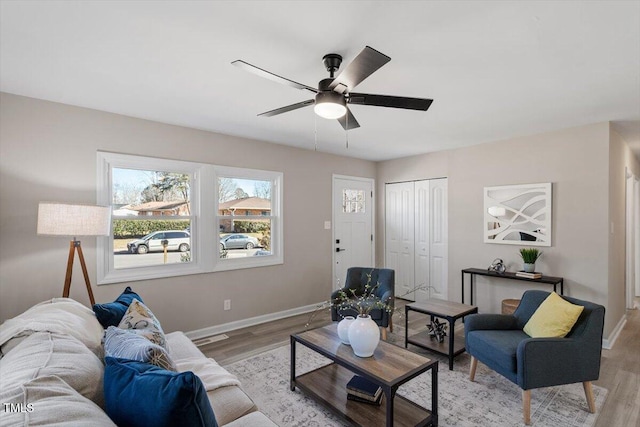 living area featuring a ceiling fan, light wood-style flooring, and baseboards