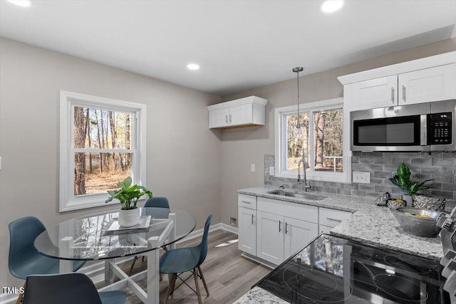 kitchen featuring tasteful backsplash, white cabinets, stainless steel microwave, light stone counters, and a sink