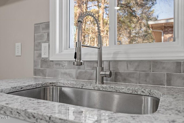 interior details with backsplash, a sink, and light stone countertops