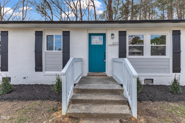 view of exterior entry with crawl space and brick siding