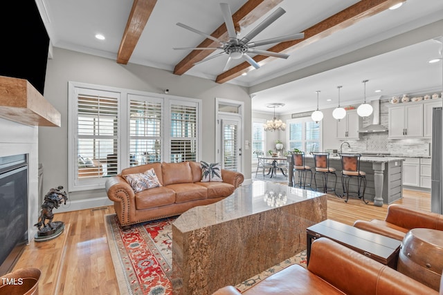 living room with ceiling fan with notable chandelier, ornamental molding, beam ceiling, and light hardwood / wood-style floors