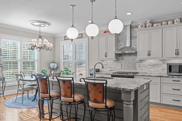 kitchen with wall chimney exhaust hood, sink, decorative light fixtures, appliances with stainless steel finishes, and a kitchen island with sink