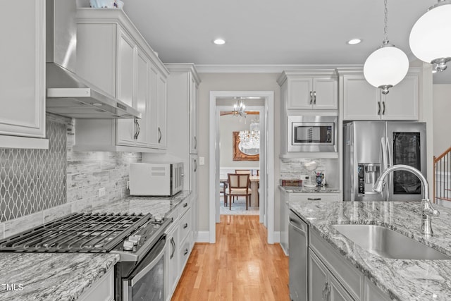 kitchen with sink, white cabinetry, hanging light fixtures, stainless steel appliances, and wall chimney range hood