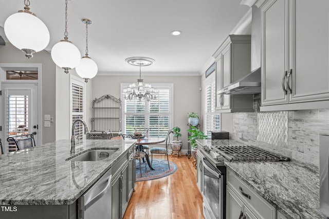 kitchen with sink, stainless steel appliances, ornamental molding, a center island with sink, and decorative light fixtures