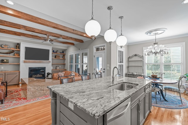 kitchen with hanging light fixtures, an island with sink, sink, and stainless steel dishwasher