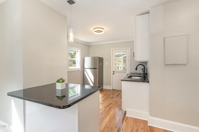 kitchen with sink, decorative light fixtures, stainless steel fridge, kitchen peninsula, and white cabinets