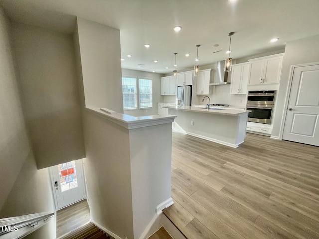 kitchen featuring hanging light fixtures, stainless steel appliances, white cabinets, and wall chimney exhaust hood