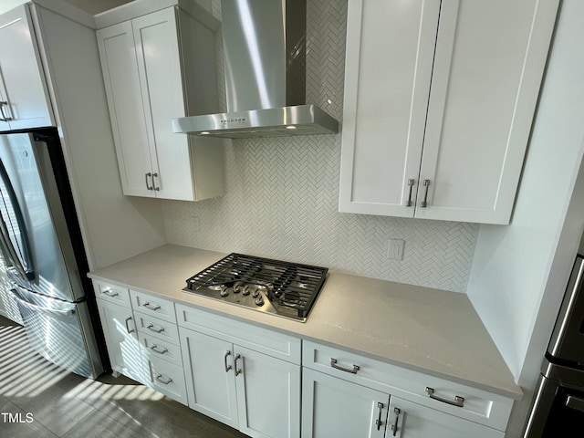 kitchen featuring appliances with stainless steel finishes, backsplash, light stone countertops, white cabinets, and wall chimney exhaust hood