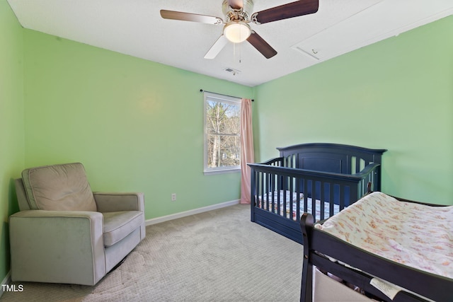 bedroom featuring a nursery area, ceiling fan, and light colored carpet