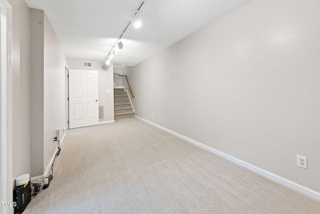 basement with rail lighting and light carpet