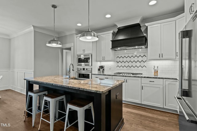 kitchen with white cabinetry, sink, hanging light fixtures, stainless steel appliances, and custom range hood