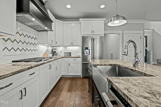 kitchen featuring appliances with stainless steel finishes, white cabinetry, light stone counters, decorative light fixtures, and custom exhaust hood