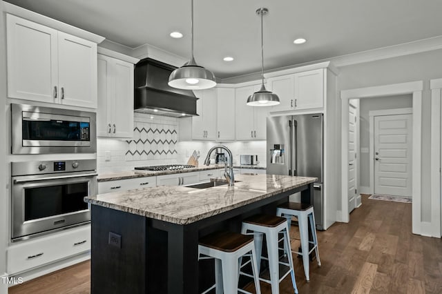 kitchen featuring appliances with stainless steel finishes, white cabinetry, an island with sink, sink, and custom exhaust hood