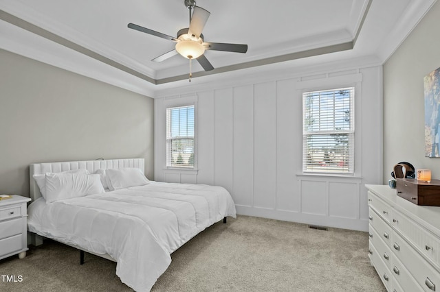 bedroom with crown molding, light colored carpet, a raised ceiling, and multiple windows