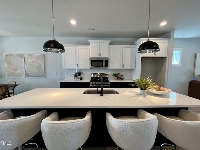 kitchen with a sink, stainless steel appliances, visible vents, white cabinetry, and pendant lighting