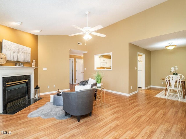 living room featuring ceiling fan, lofted ceiling, a fireplace, and light hardwood / wood-style flooring