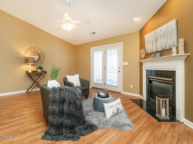 living room featuring lofted ceiling, light hardwood / wood-style flooring, a tile fireplace, and ceiling fan