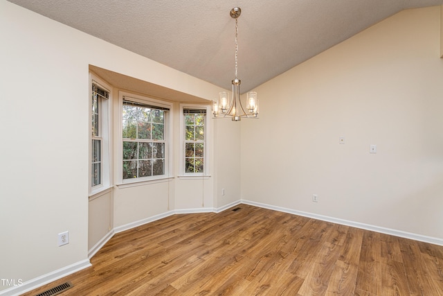 unfurnished dining area featuring hardwood / wood-style flooring, an inviting chandelier, vaulted ceiling, and a textured ceiling