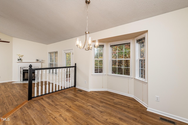 unfurnished room with an inviting chandelier, a fireplace, dark hardwood / wood-style flooring, and a textured ceiling