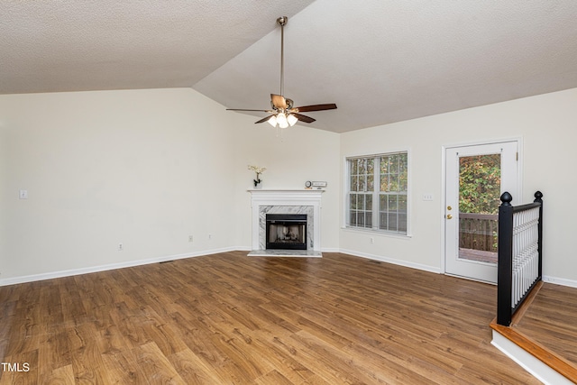 unfurnished living room featuring wood-type flooring, lofted ceiling, ceiling fan, a premium fireplace, and a textured ceiling