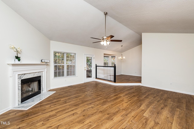 unfurnished living room featuring hardwood / wood-style floors, a high end fireplace, a textured ceiling, ceiling fan with notable chandelier, and vaulted ceiling