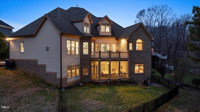 back house at dusk with a lawn and a balcony