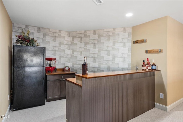 kitchen with a breakfast bar, dark brown cabinets, black fridge, light carpet, and kitchen peninsula