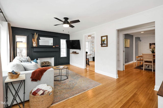 living room featuring crown molding, ceiling fan, wood-type flooring, and a fireplace