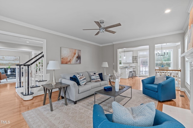 living room with ceiling fan with notable chandelier, ornamental molding, and light wood-type flooring