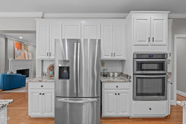 kitchen with light stone countertops, appliances with stainless steel finishes, ornamental molding, and white cabinets