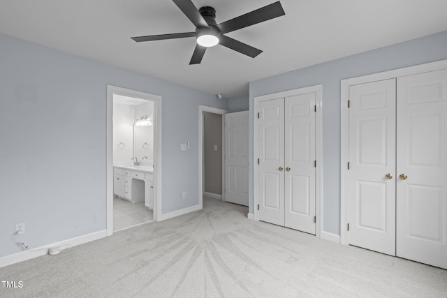 unfurnished bedroom featuring two closets, sink, light colored carpet, ceiling fan, and ensuite bath