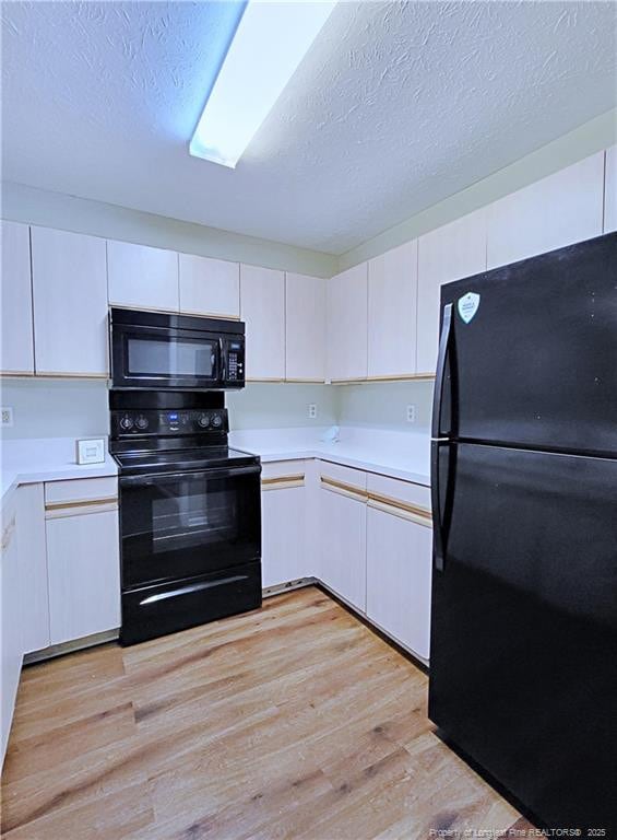 kitchen with light hardwood / wood-style flooring, white cabinets, a textured ceiling, and black appliances