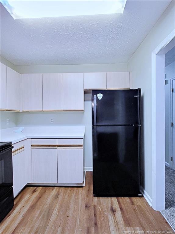 kitchen with white cabinetry, a textured ceiling, light wood-type flooring, black refrigerator, and stove