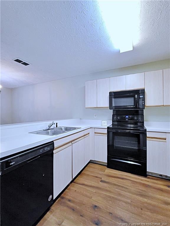 kitchen with sink, white cabinetry, black appliances, a textured ceiling, and light wood-type flooring