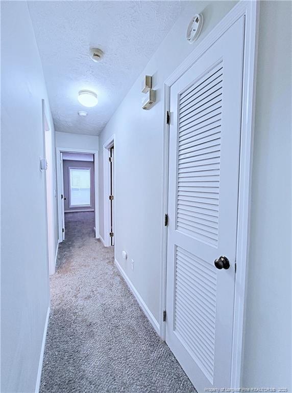 hallway with light carpet and a textured ceiling