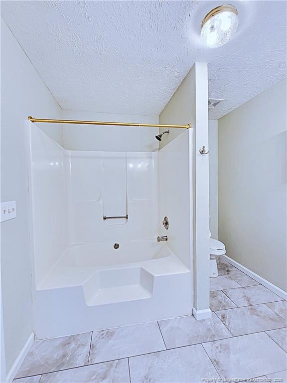 bathroom featuring tile patterned floors, shower / washtub combination, toilet, and a textured ceiling