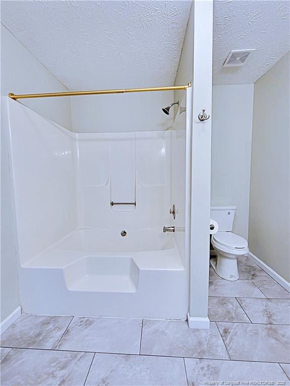 bathroom featuring tile patterned flooring,  shower combination, a textured ceiling, and toilet