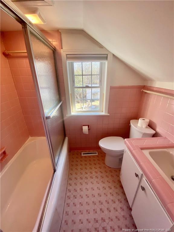 full bathroom featuring lofted ceiling, combined bath / shower with glass door, tile walls, vanity, and toilet