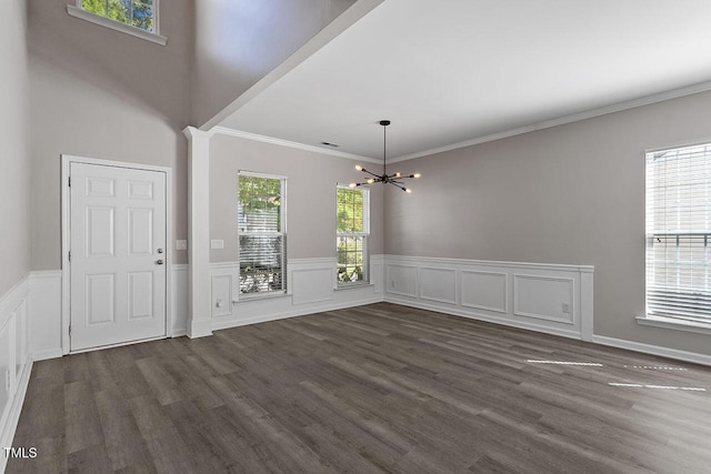 unfurnished dining area featuring dark hardwood / wood-style flooring, a notable chandelier, a wealth of natural light, and ornamental molding