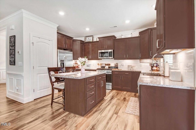 kitchen with a kitchen island, appliances with stainless steel finishes, a breakfast bar, light stone counters, and light hardwood / wood-style flooring