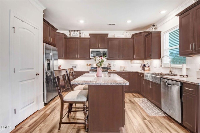 kitchen featuring appliances with stainless steel finishes, sink, a breakfast bar area, a center island, and light stone counters