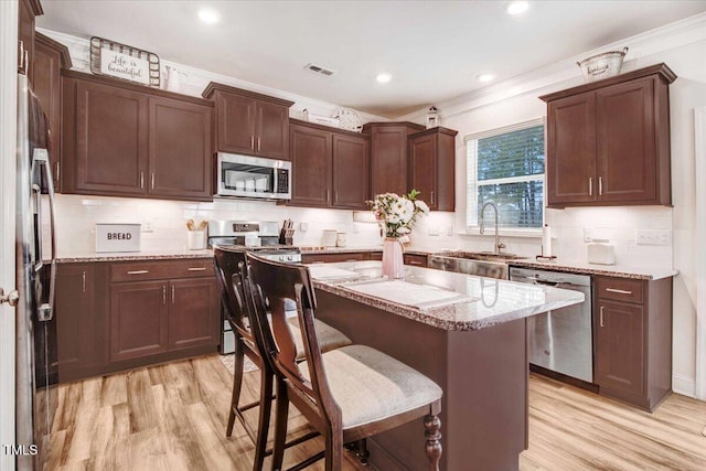 kitchen featuring sink, light hardwood / wood-style flooring, appliances with stainless steel finishes, a center island, and light stone counters