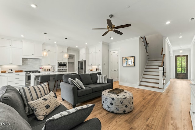 living room featuring ceiling fan, ornamental molding, sink, and light wood-type flooring